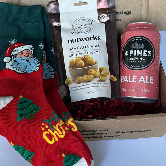 Gift box with a pair of Christmas-themed socks, macadamia nuts, and a beer can on a white background.