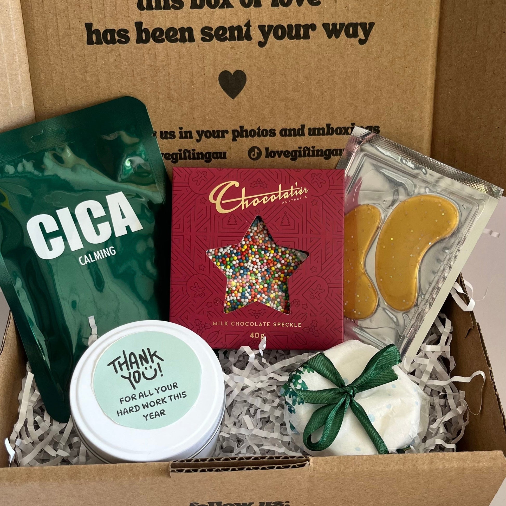 Box of assorted items including a CICA product, a chocolate bar, and other small items with a message on the box.