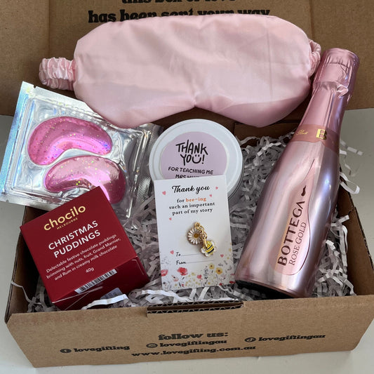 Gift box with pink sleep mask, chocolate, and bottle of champagne on a white background