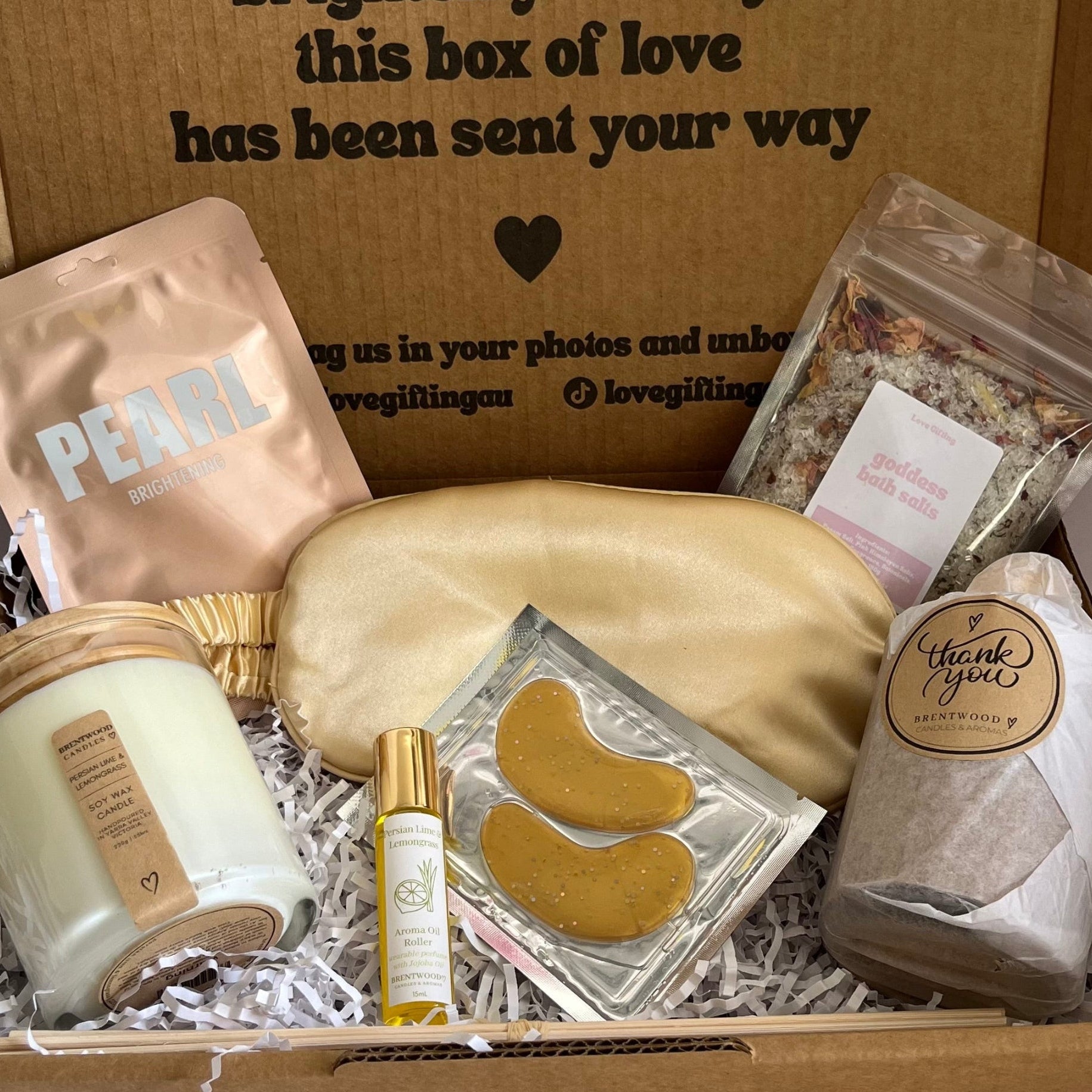 Gift box with self-care items including a candle, eye masks, and a pouch on a white background.