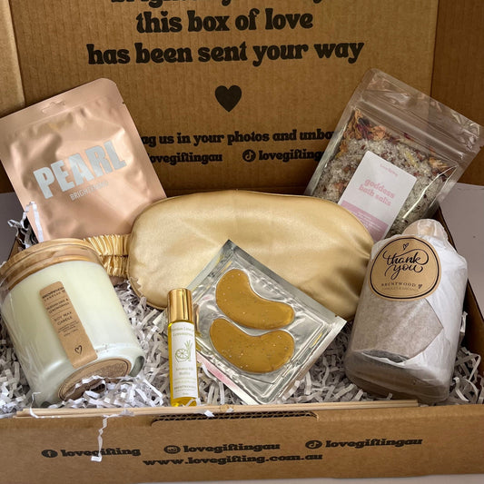 Gift box with self-care items including a candle, eye masks, and a pouch on a white background.