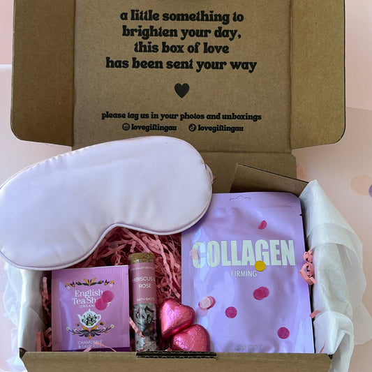 Open box containing a purple satin sleep mask, Lapcos Sheet mask , English Tea , Bath Salt Shot and Pink chocolate hearts