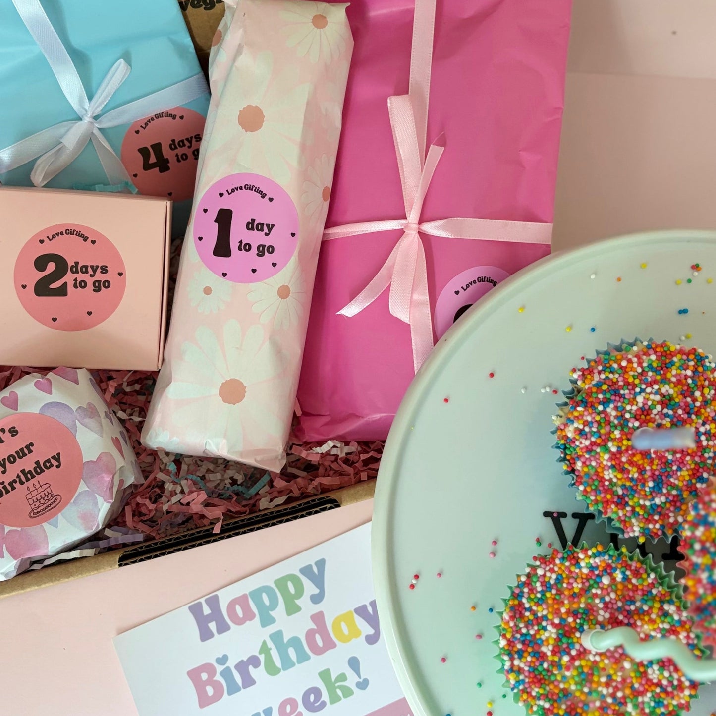 Gifts and birthday items including a box, card, and small wrapped presents on a pink surface.