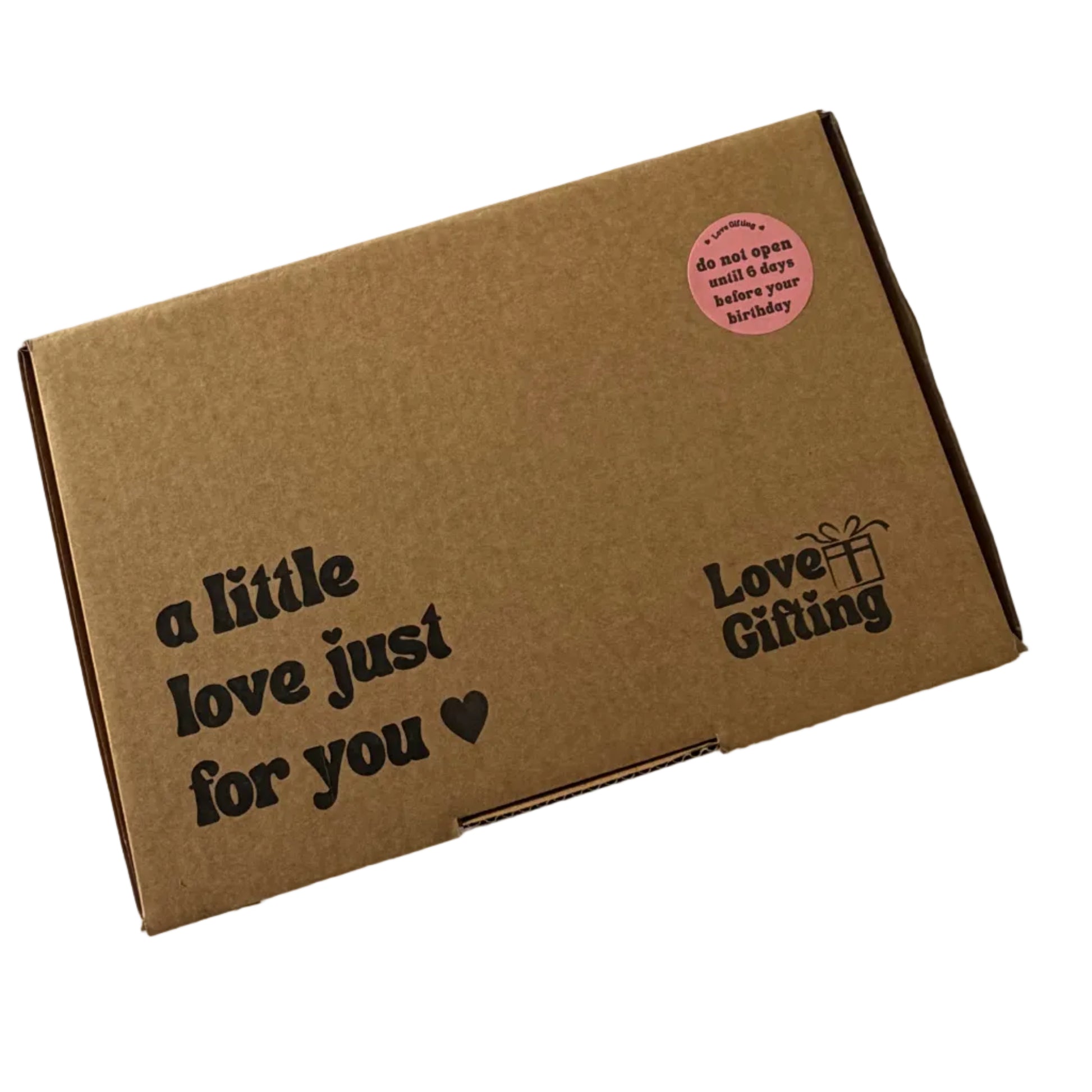 A brown cardboard gift box with black printed text reading 'a little love just for you' and 'Love Gifting', plus a small pink circular sticker, photographed on a white surface.