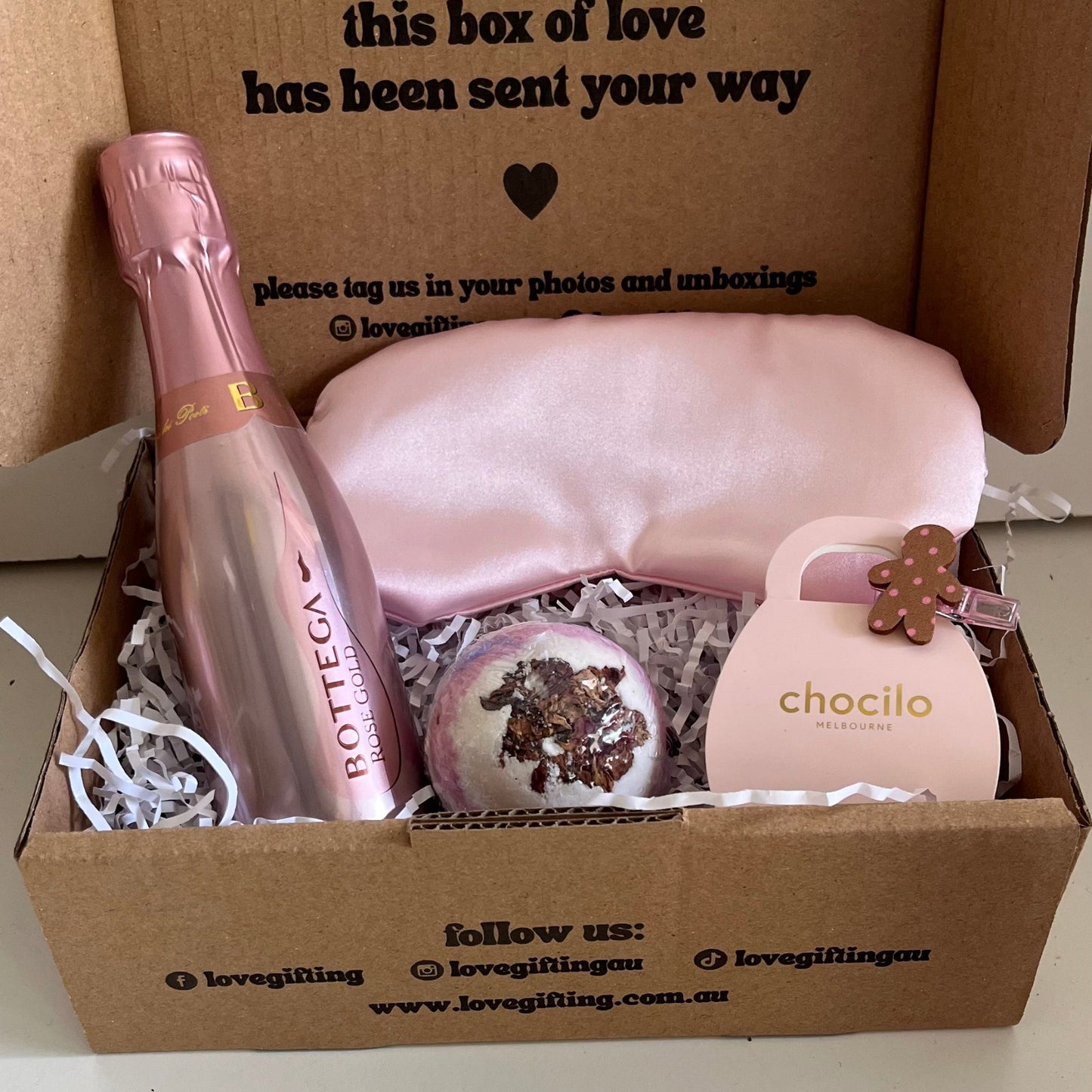 Gift box with a bottle of Prosecco, a bag, and a small item, with text on the box.
