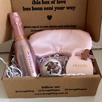 Gift box with a bottle of Prosecco, a bag, and a small item, with text on the box.