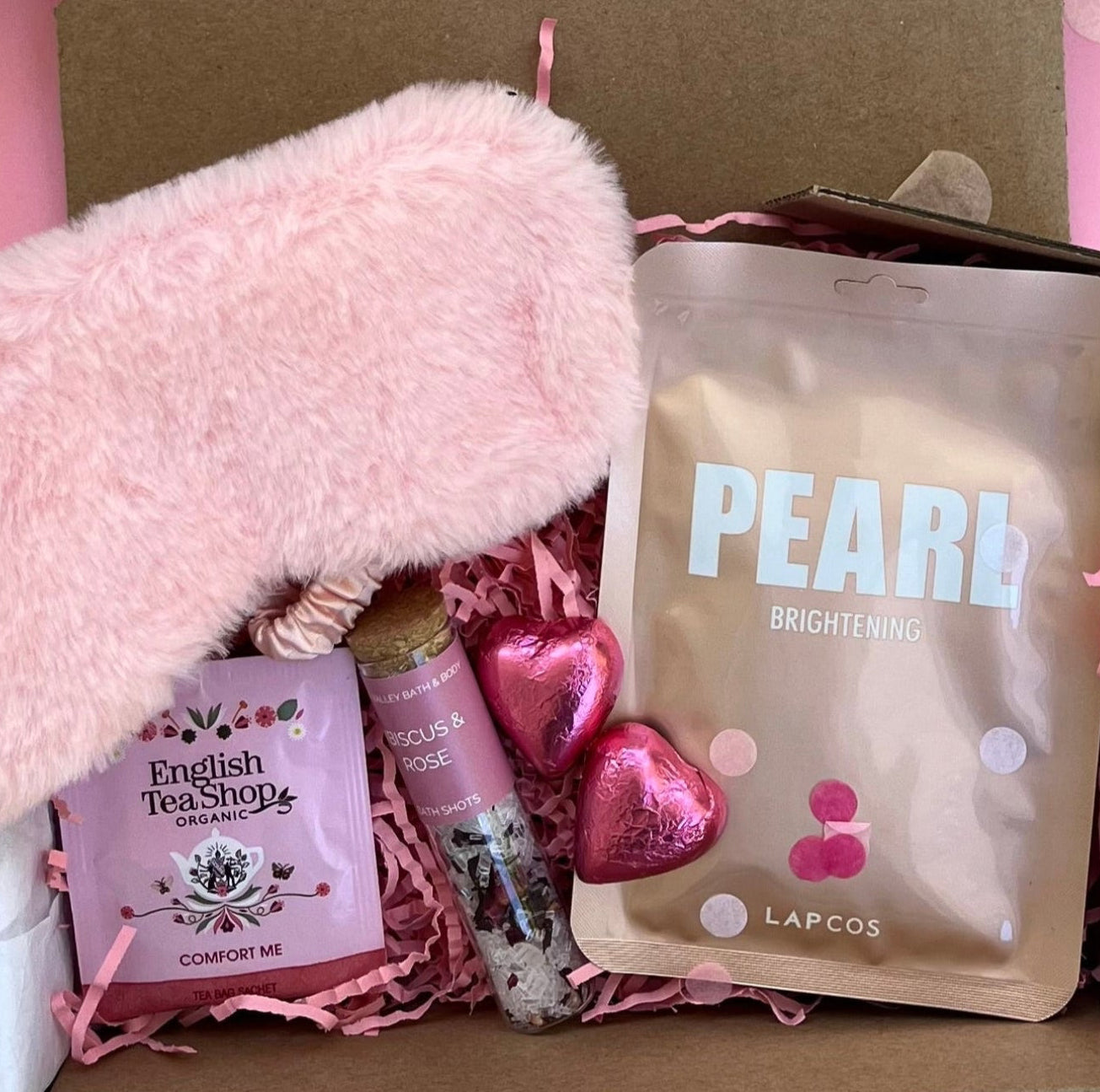 Gift box with pink fluffy item, lip balm, and skincare product on a pink background
