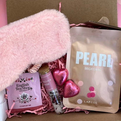Gift box with pink fluffy item, lip balm, and skincare product on a pink background
