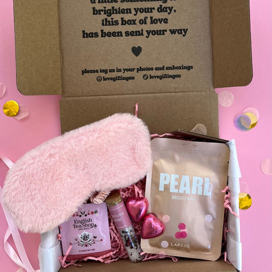 Gift box with pink fluffy item, lip balm, and skincare product on a pink background