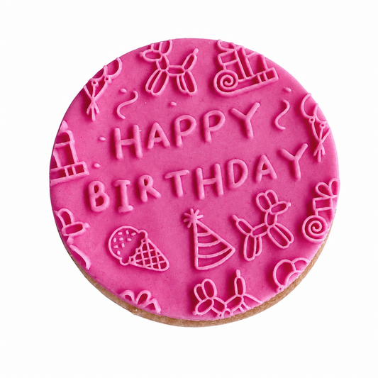 A round birthday cookie topped with bright pink icing, decorated with embossed 'HAPPY BIRTHDAY' text and balloon-themed party icons, shown on a plain white background.