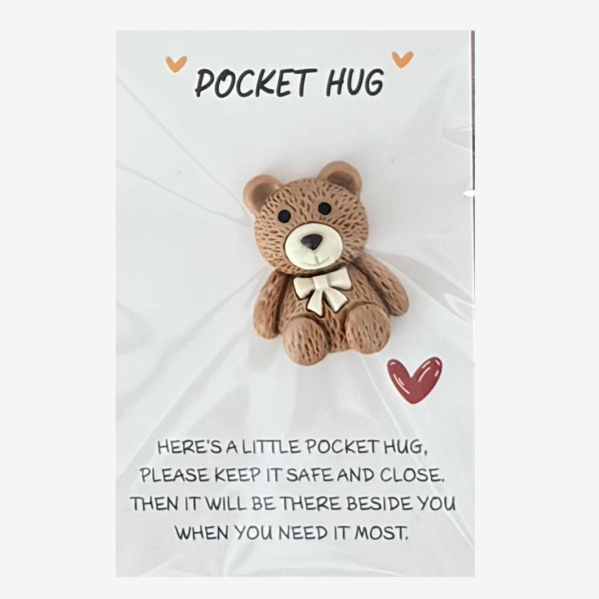 Small teddy bear with a gold bow on a white card with text, labeled 'Pocket Hug'.