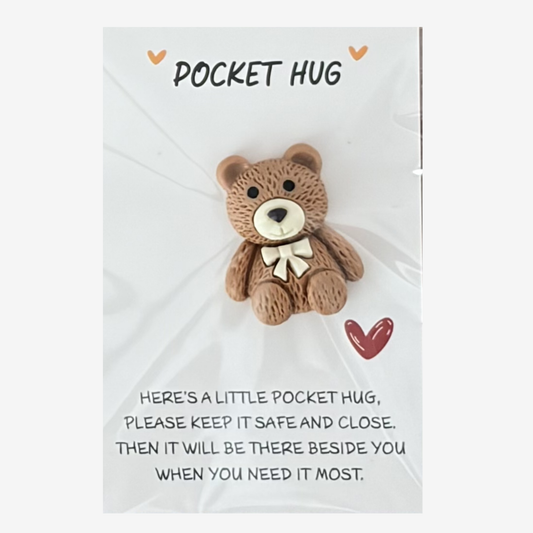 Small teddy bear with a gold bow on a white card with text, labeled 'Pocket Hug'.