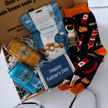 A Father's Day gift box filled with treats and a pair of novelty socks. The open brown cardboard box has printed text on the inside lid.