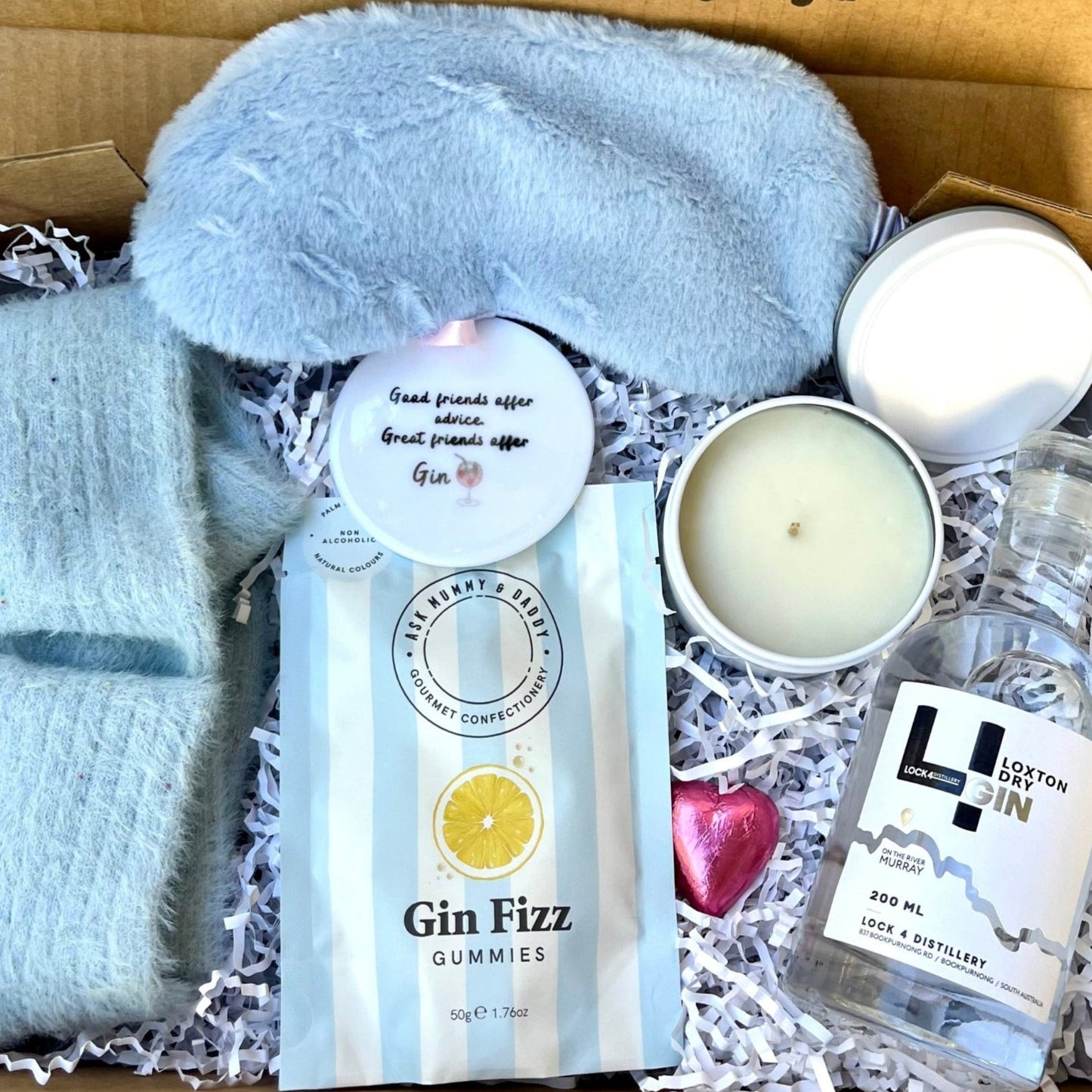 Gift box with light blue socks, Gin Fizz gummies, and other items, with a message on the lid.