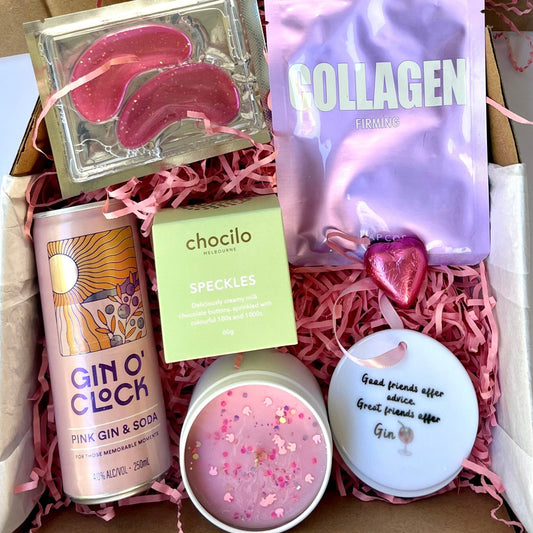 Gift box with various items including a gin bottle, snacks, and a candle on a white background.