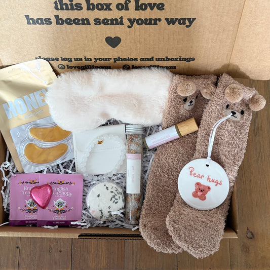 Gift box with various items including socks, a card, and a small bag on a wooden surface.