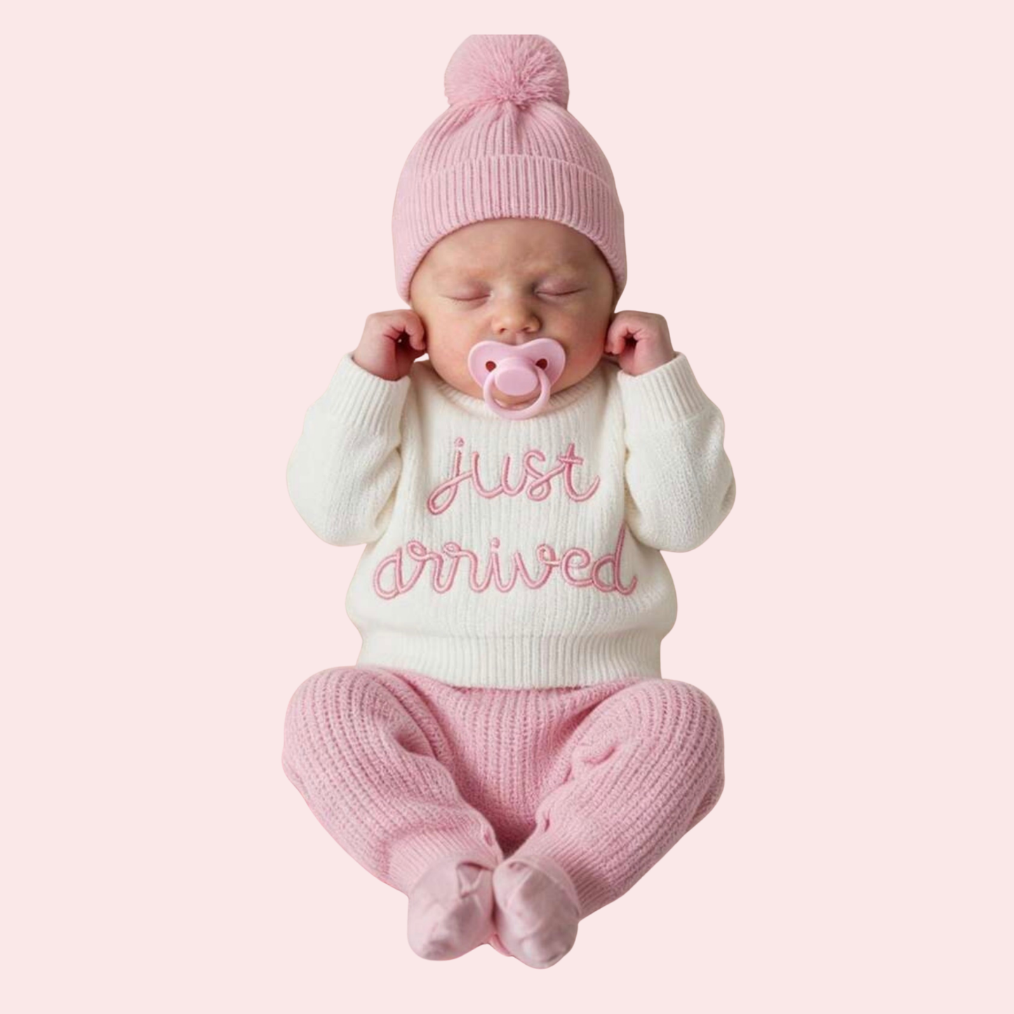 Newborn baby in pink and white outfit with 'Just arrived' text on a light pink background