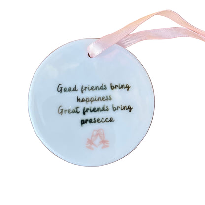 Round white ornament with text and a pink ribbon on a wooden surface
