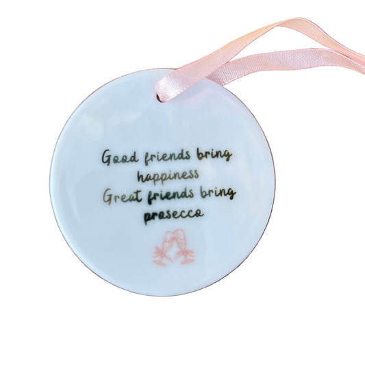 Round white ornament with text and a pink ribbon on a wooden surface