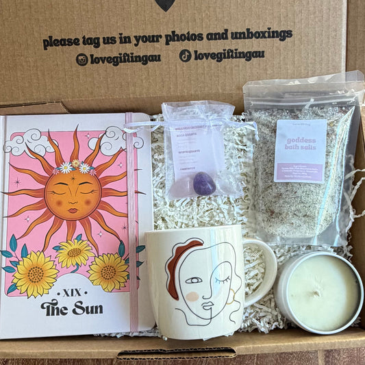 Box of goddess love with a mug, card, and candle on a wooden surface