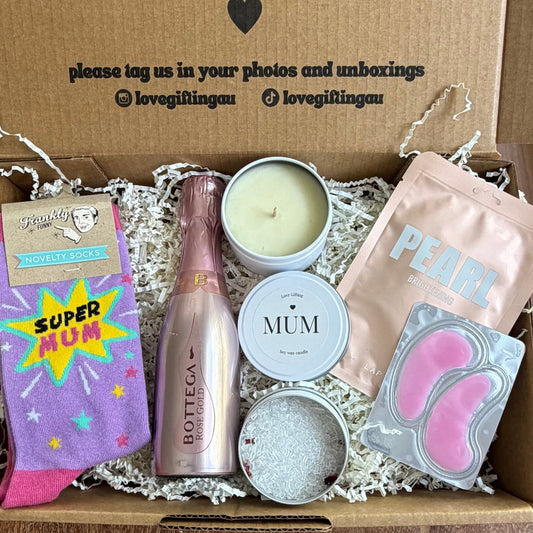 Gift box with various items including a bottle, candles, and cards on a wooden surface.
