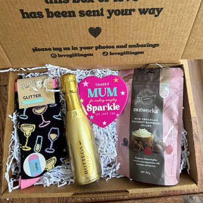 Gift box with various items including a bottle, card, and snacks on a wooden surface.