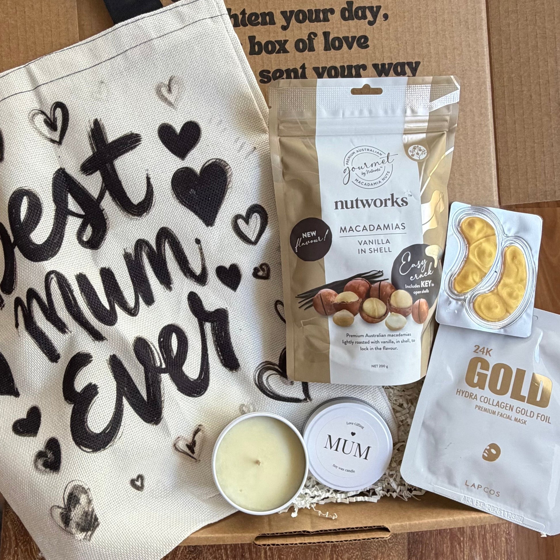 Gift box with 'Best Mum Ever' towel, Nutworks macadamias, Gold Collagen, and a candle on a wooden surface.