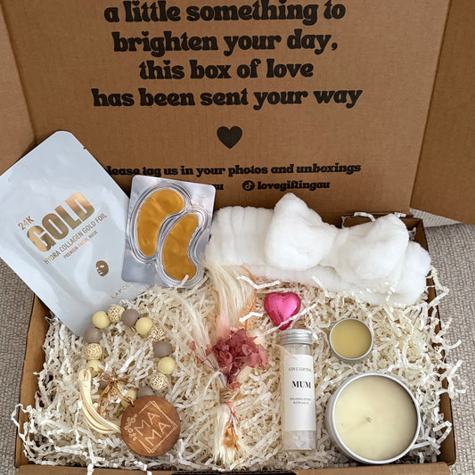 Gift box with various items including a candle, soap, and a bottle, with a message on the box.