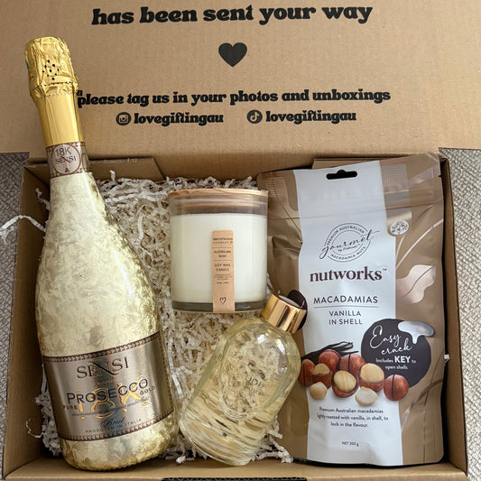Gift box with champagne, candle, and snacks on a gray surface