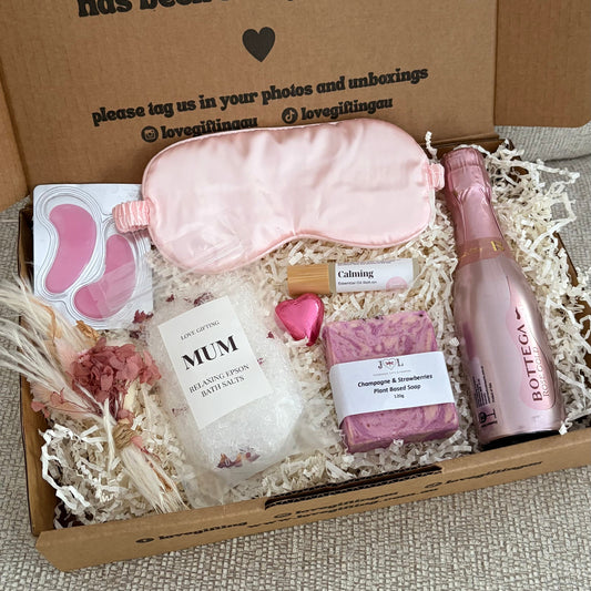 Gift box with self-care items including a sleep mask, eye masks, and a bottle of lotion on a textured surface.