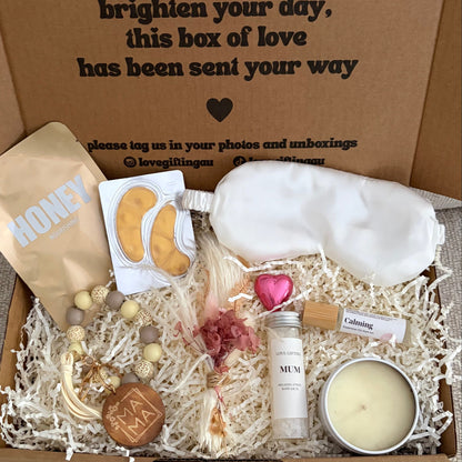 Box of assorted items including a candle, cookies, and a bottle, with a message on the lid.