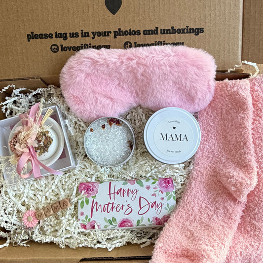 Mothers Day gift box with pink fuzzy socks, a small plant, and a card inside, on a wooden surface.