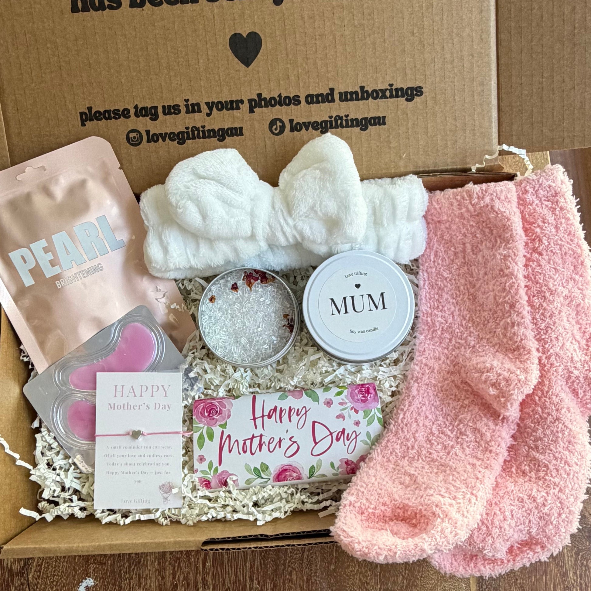 Mothers day Gift box with pink socks, a card, and other items on a wooden surface.