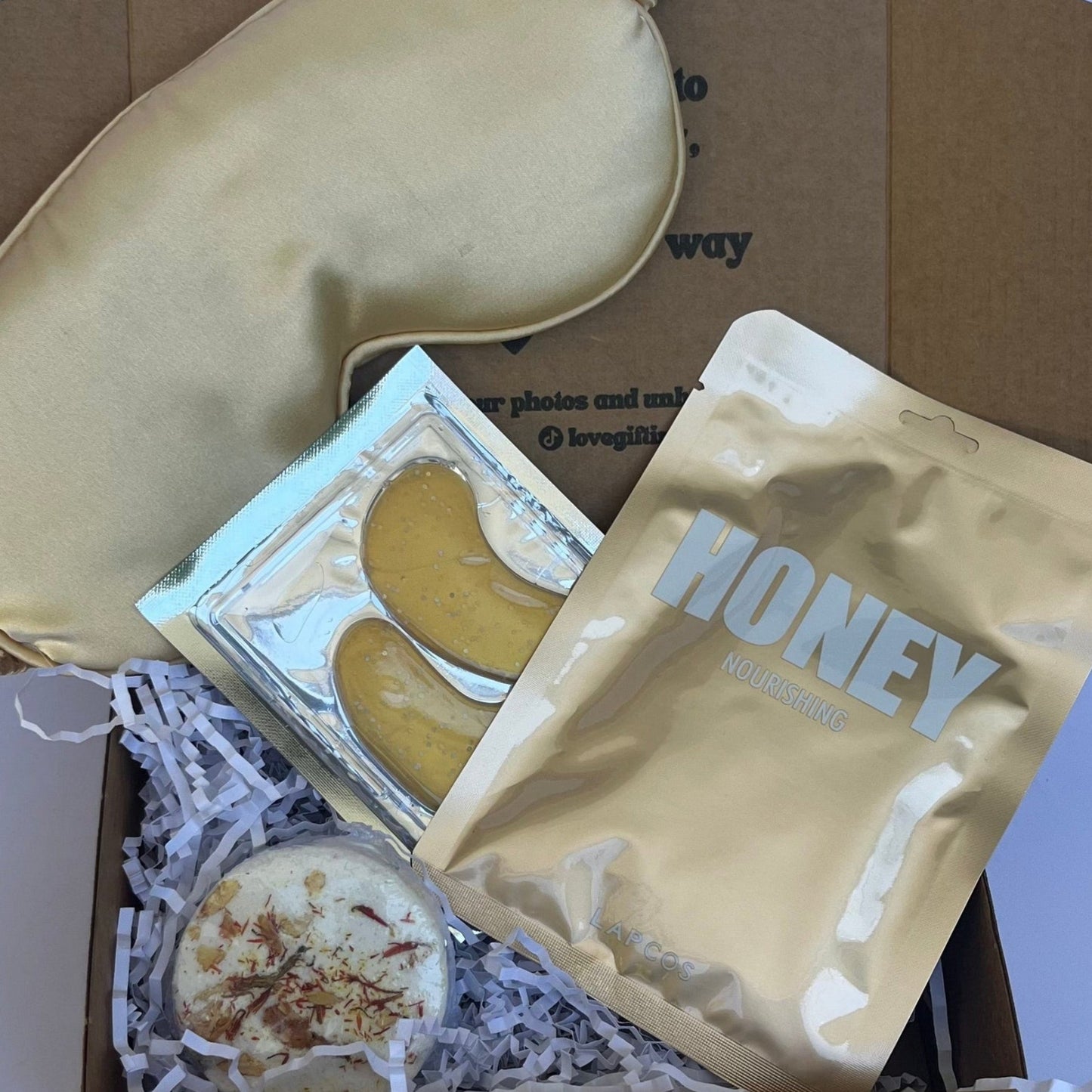 Gold sleep mask and honey packets in a box on a white background
