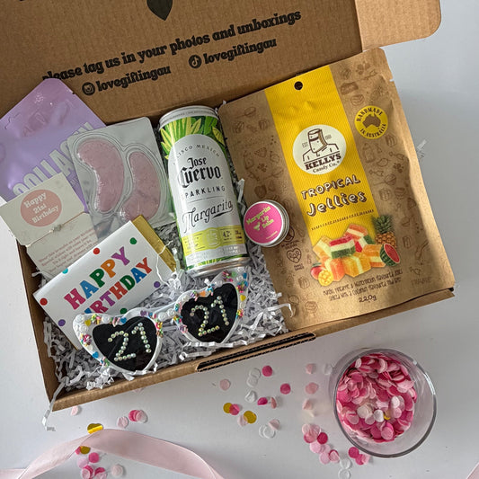 A curated gift box filled with assorted treats and accessories,  the contents include a purple envelope, a can of margarita , margarita lipbalm, Tropical gummies,  21st sunglasses, 21st bracelet, lapcos collagen facemask , under eye mask and happy birthday chocolate,