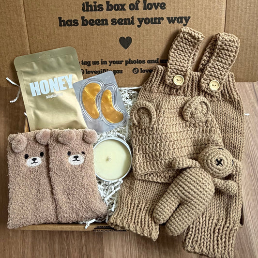 Gift box with baby items including socks, gloves, and a card on a wooden floor.