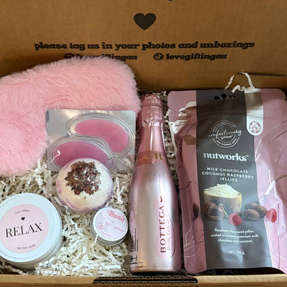 Box of self-care items including a bottle, candles, and a bag with a message on the box.