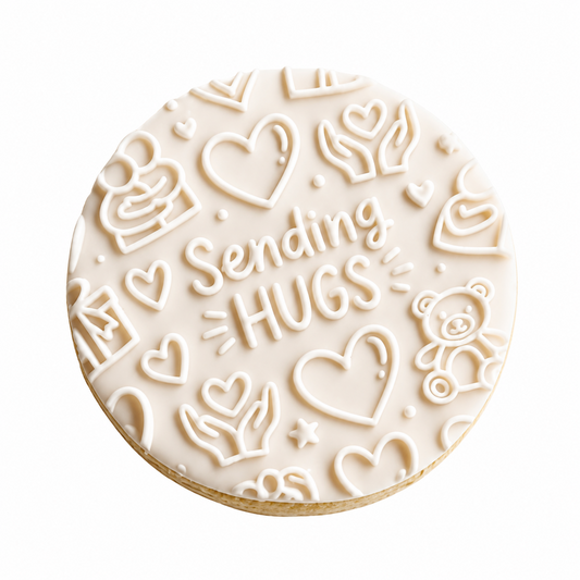 A round white-frosted cookie decorated with embossed hearts, hands, a teddy bear, and the words 'Sending HUGS' in script, shown on a plain white background.