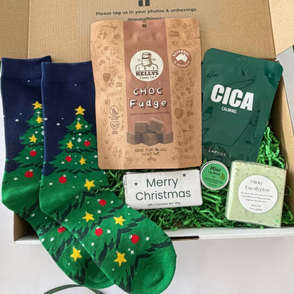 Christmas Comfort & Treats men's Christmas gift box featuring Christmas tree socks, Kelly's chocolate fudge, LAPCOS face mask, Merry Christmas milk chocolate, mint lip balm and eucalyptus soap in festive packaging.