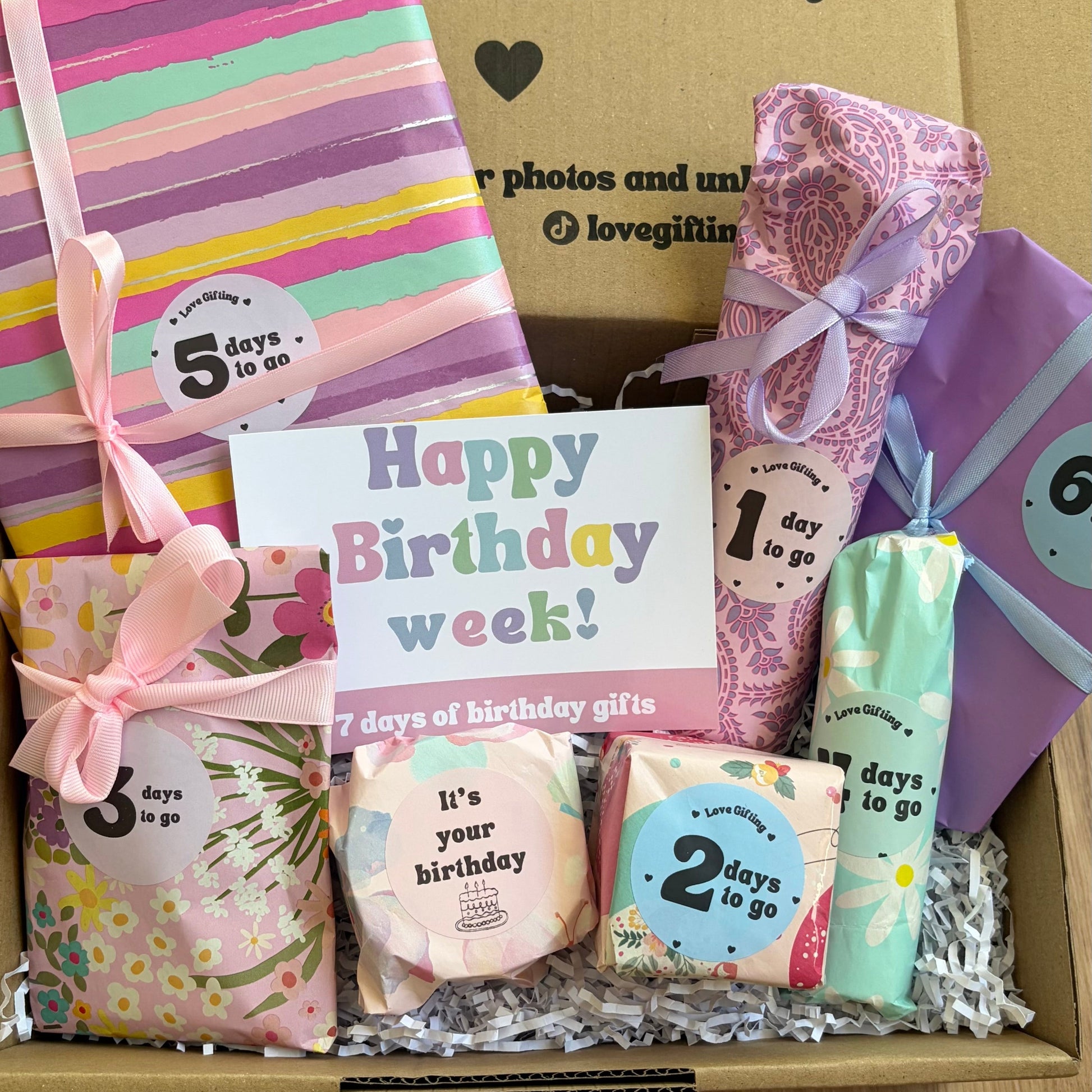 Gift box with birthday-themed items including a striped notebook, soap, and cards on a wooden surface.