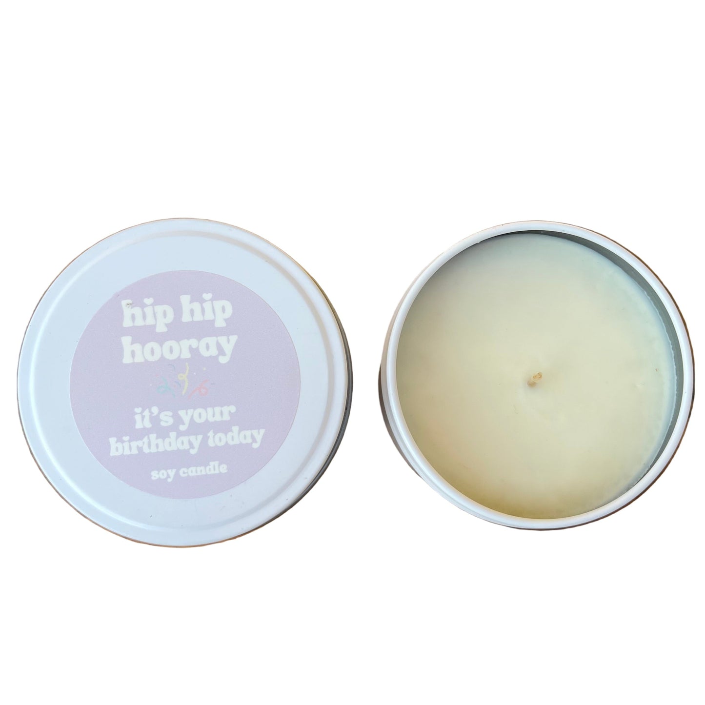 Candle in a tin with 'hip hip hooray' text on a wooden surface